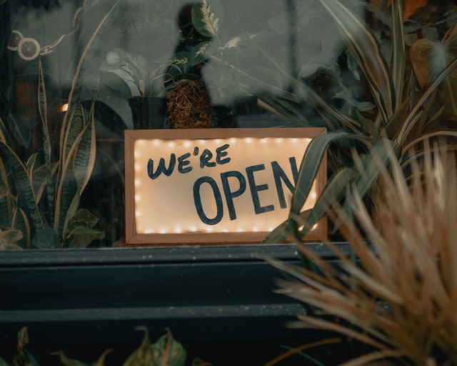 we're open sign in plant filled window