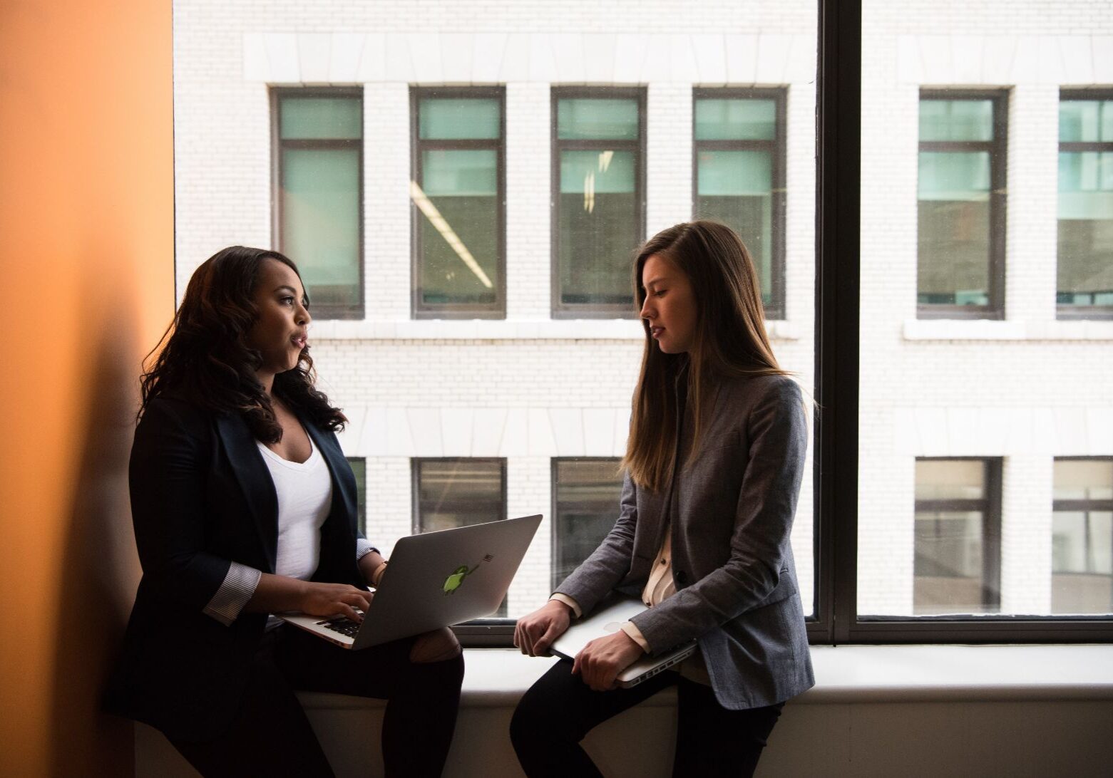 two women sitting on a windowsill having a business meeting